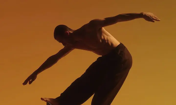 A shirtless man balancing on the top of a structure.